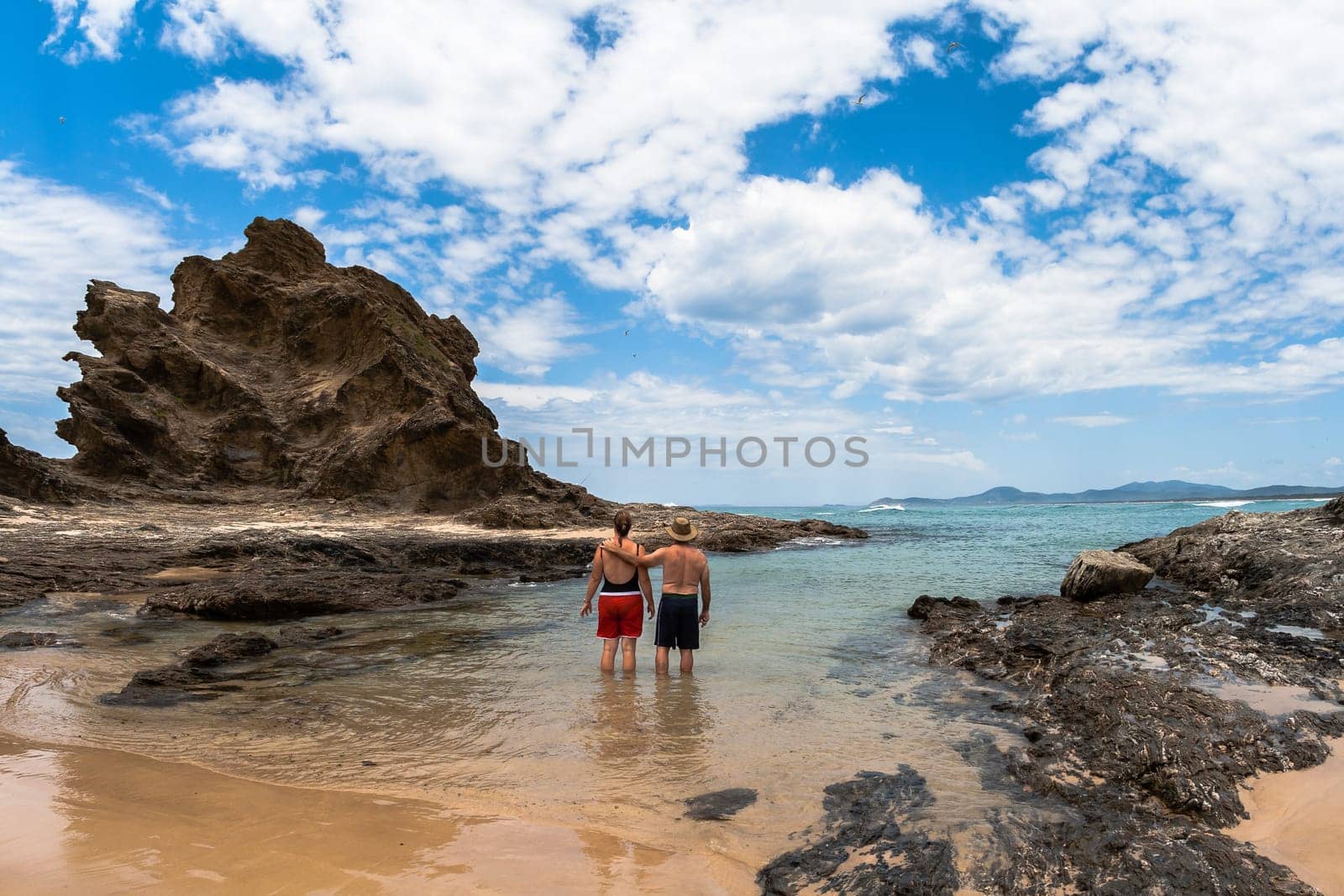 Ocean Beach blue waters and rocky headland into the scenic landscape with family in swim cove on holiday