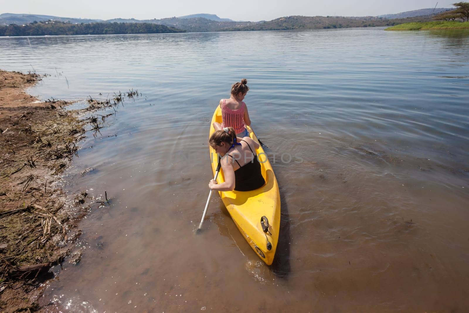 Teenage girls going out on yellow canoe to explore dam lake waters and shoreline