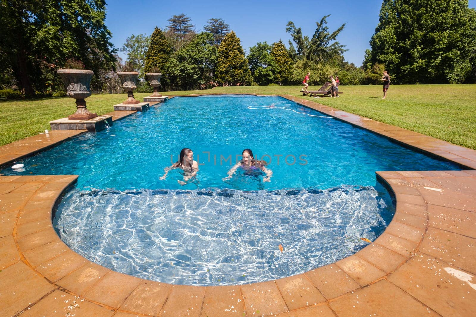 Teen girls in swimming pool with boys on grass lawn outdoors summer