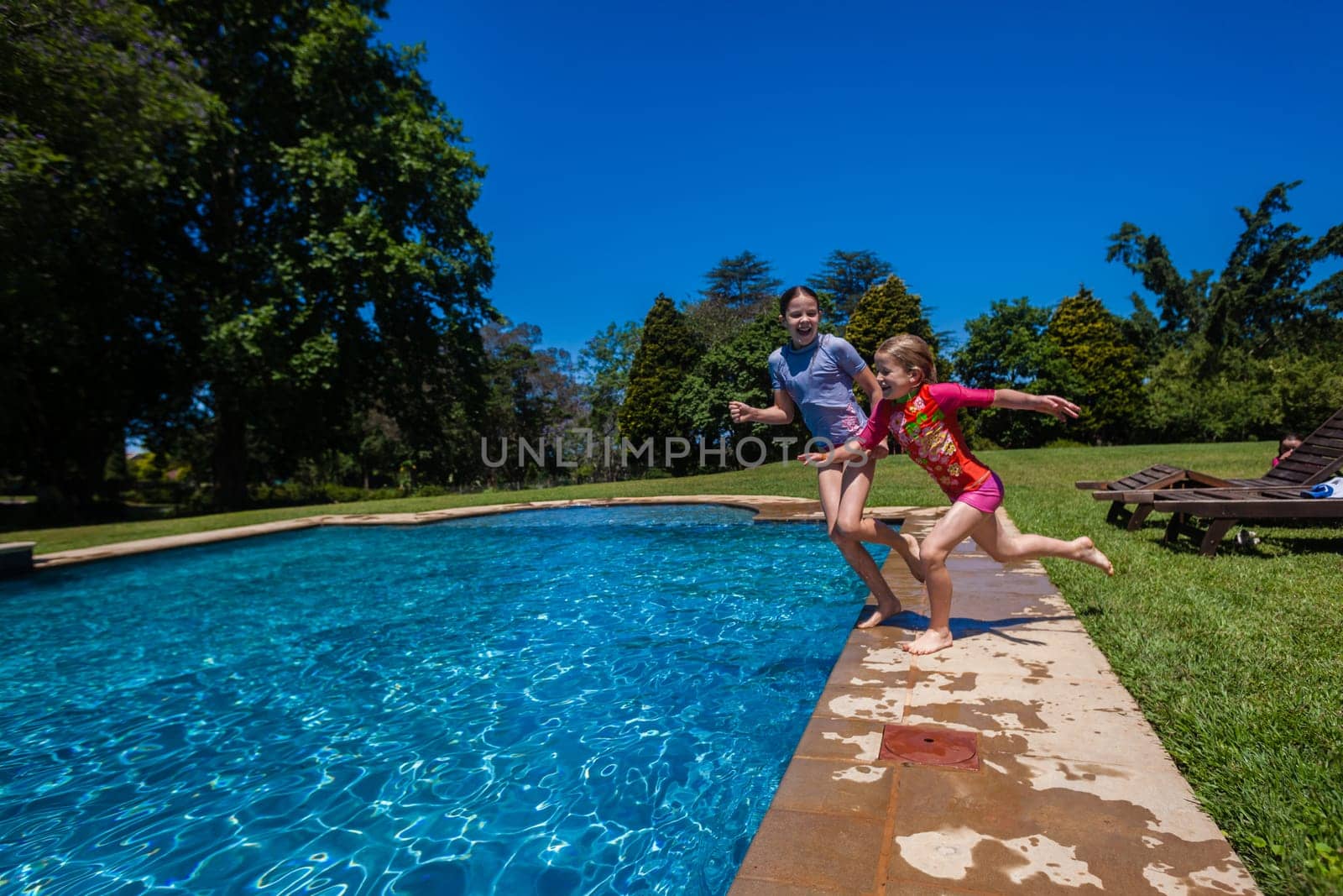 Girls at home playtime jumping into swimming pool outdoors summer