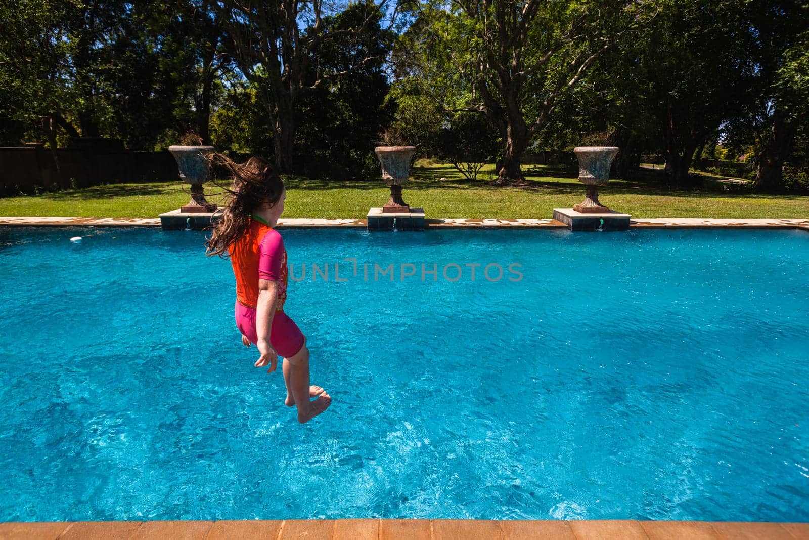Girl at home playtime jumping into swimming pool outdoors summer
