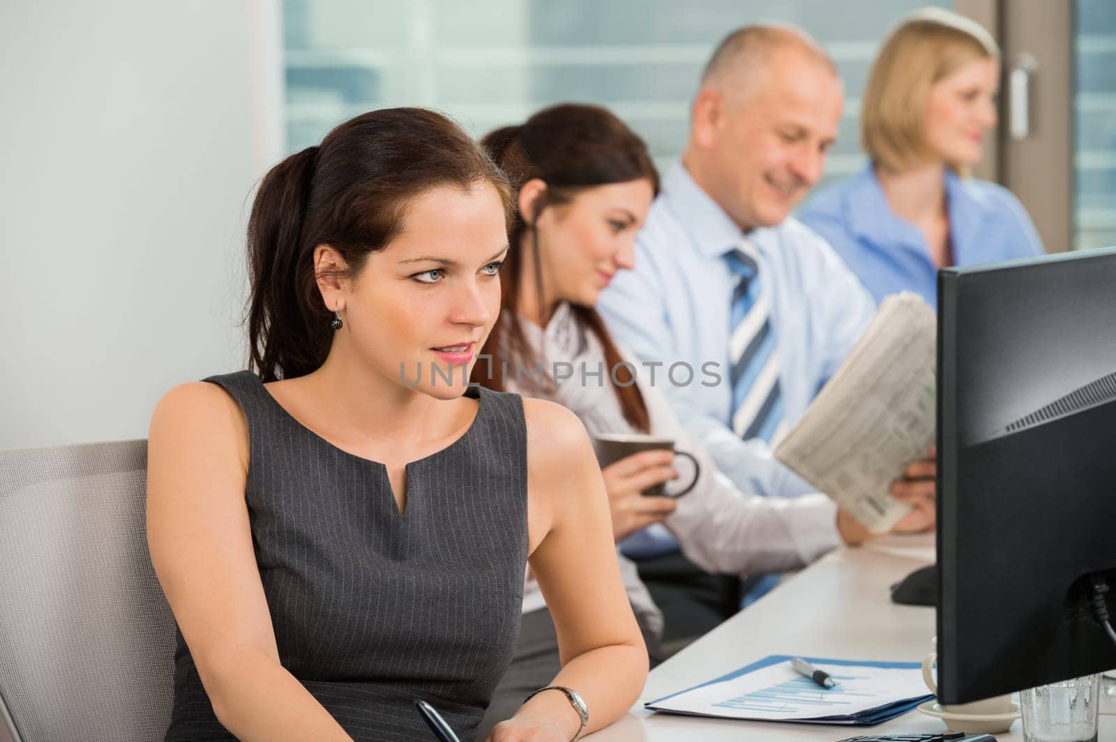 Businesswoman using computer with colleagues in background at office
