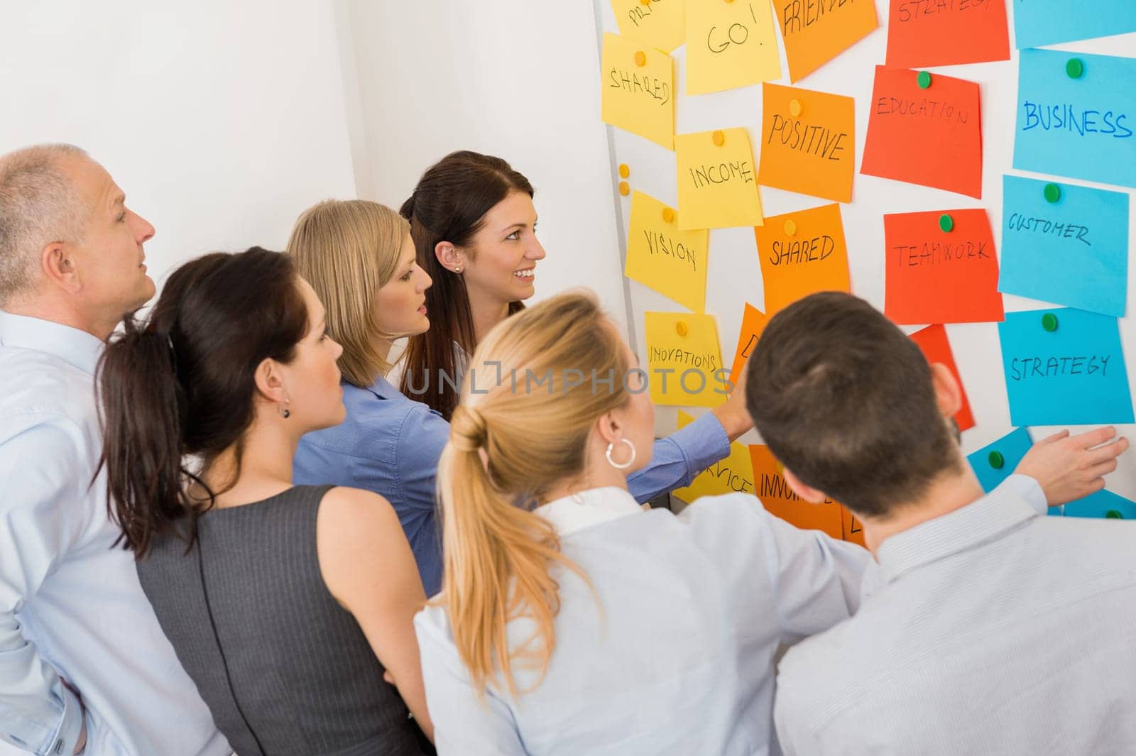Business colleagues brainstorming multicolored labels stuck on whiteboard in meeting