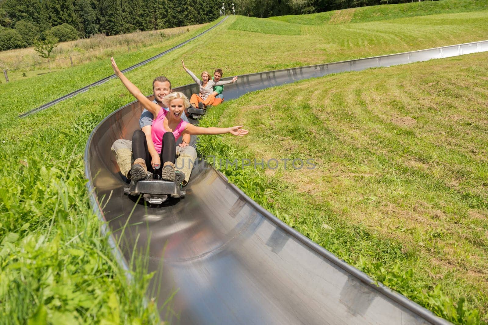 Excited young couples enjoying alpine coaster luge during summer
