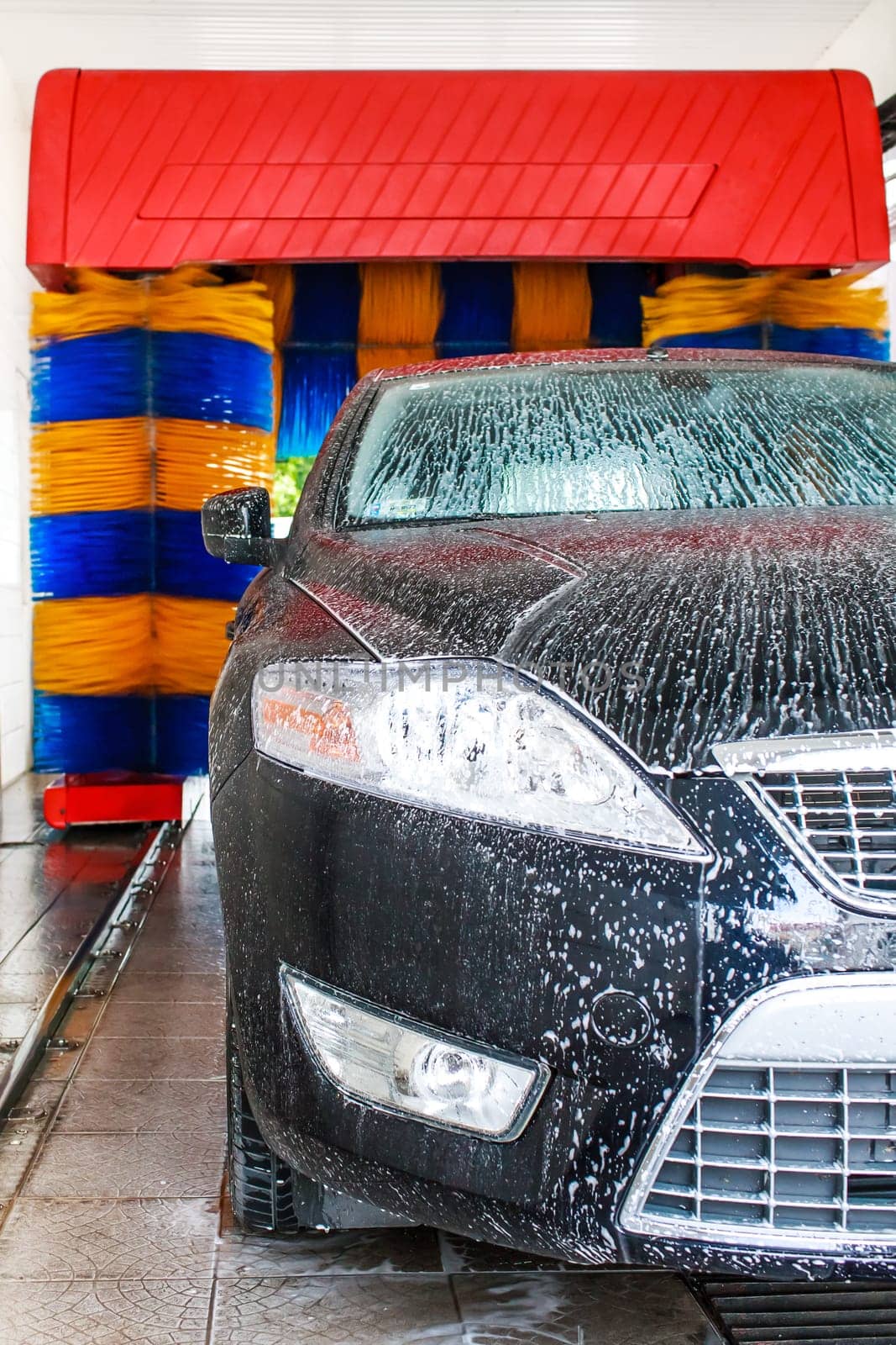 car being washed in automatic car wash,blue and yellow rotating brushes visible  unrecognizible make and model labels,model release not required.