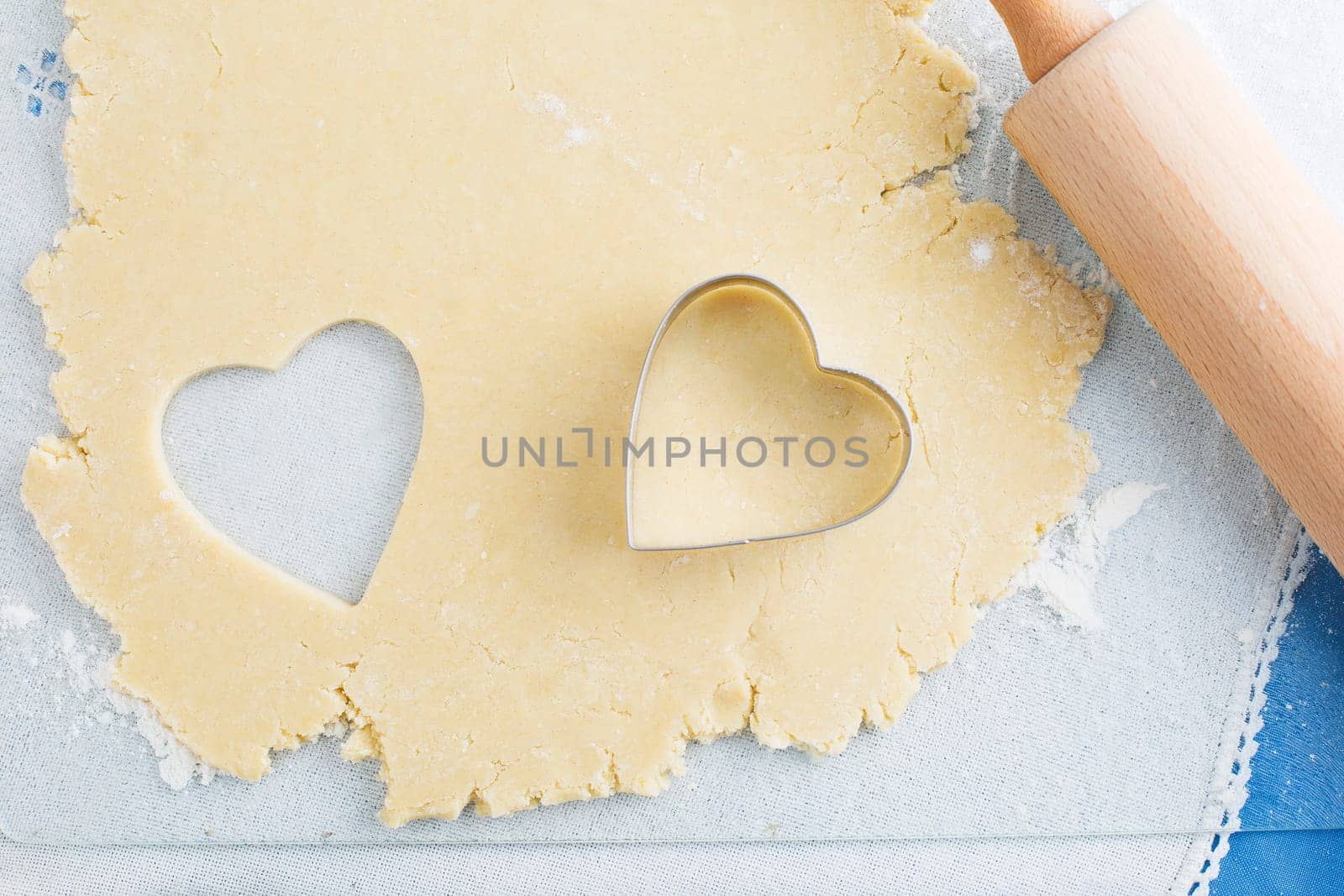 Heart shaped cookie cut out of cookie dough with cutter and rolling pin