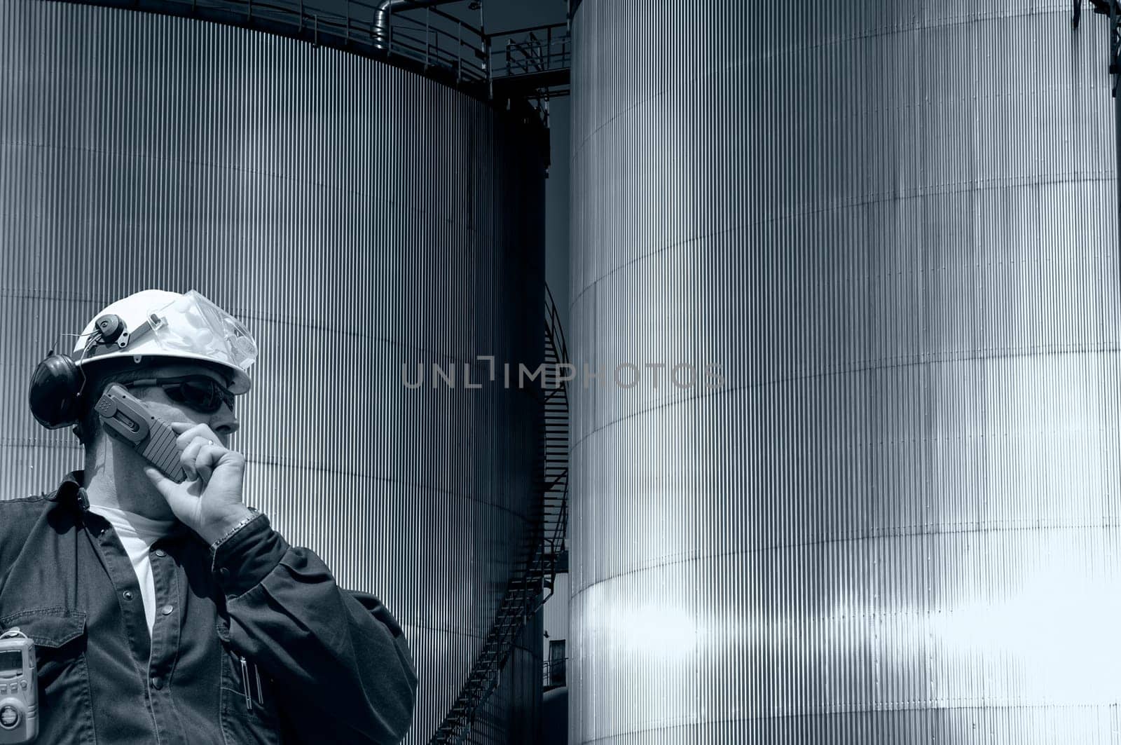 oil and gas industrial fuel storage tanks inside refinery, engineer, worker talkin in phone