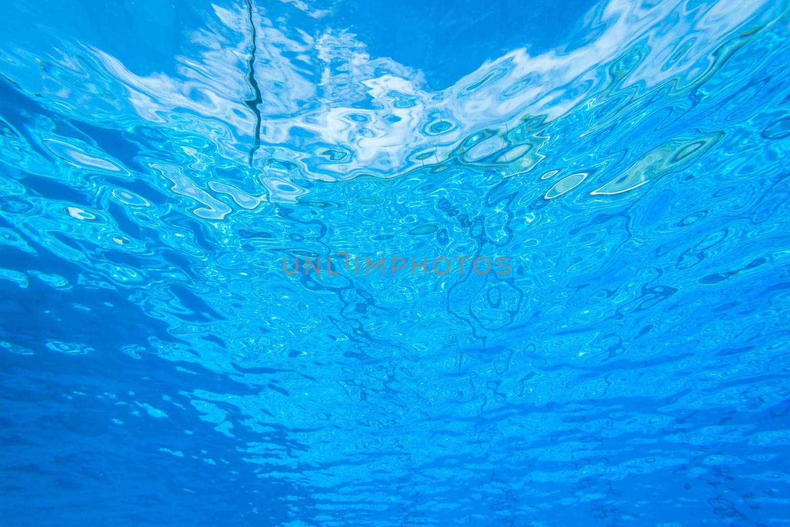 Underwater swimming pool waters towards surface and blue sky