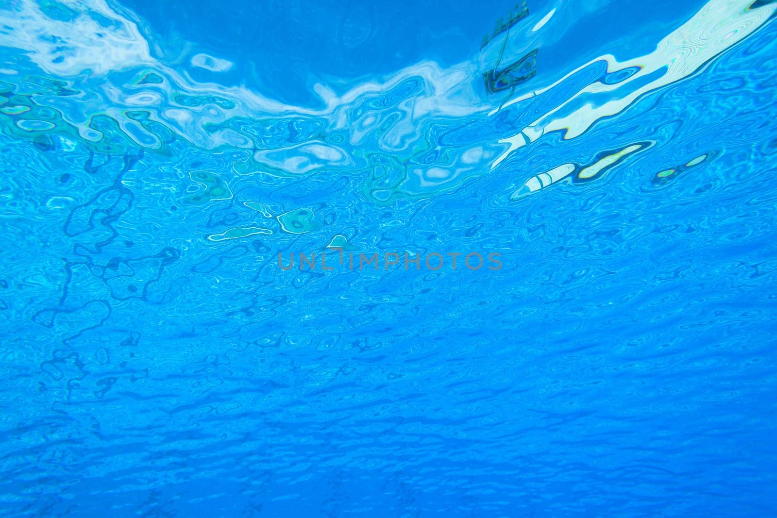 Underwater swimming pool waters towards surface and blue sky