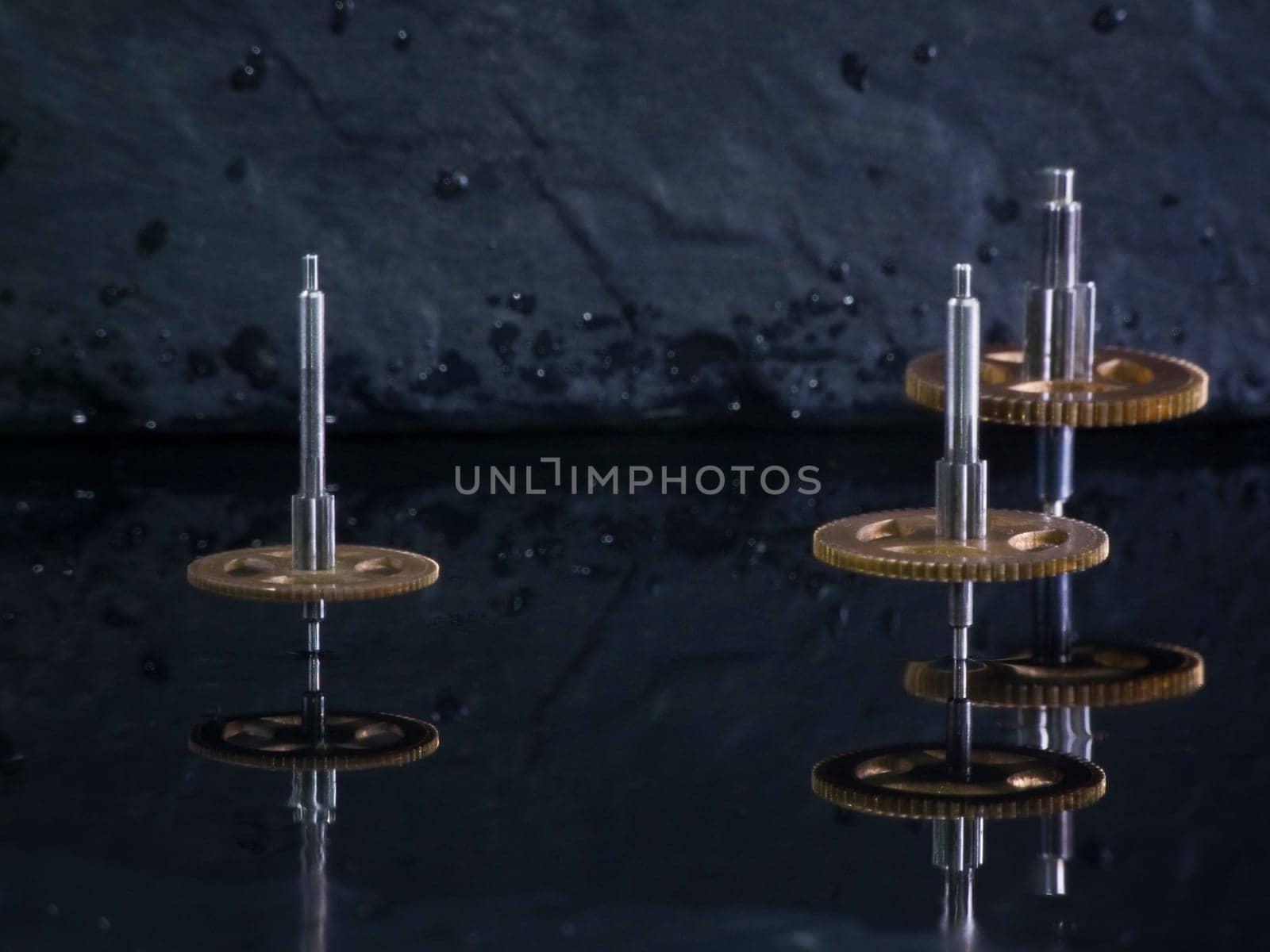 Close-up three fast-rotating gears on water-covered slate slab
