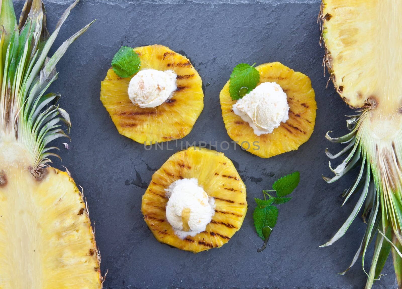 Grilled pineapple rings with ice cream balls and honey on slate plate