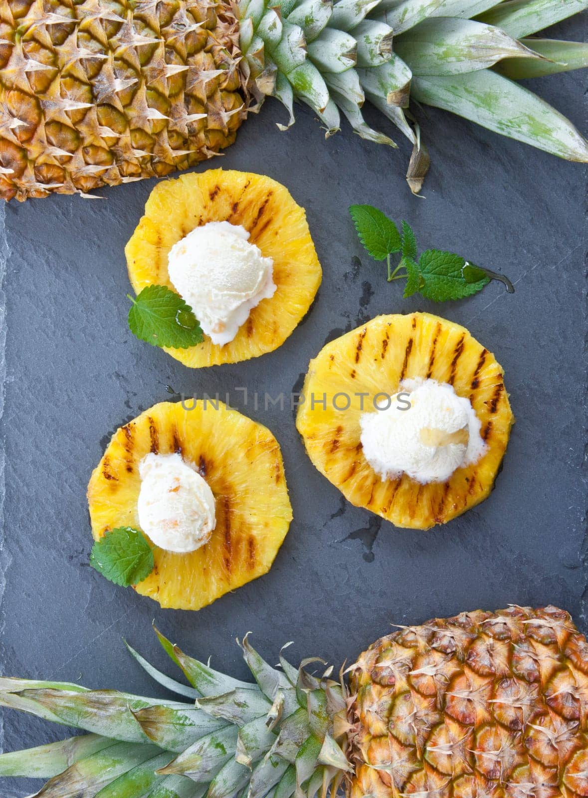 Grilled pineapple rings with ice cream balls and honey on slate plate