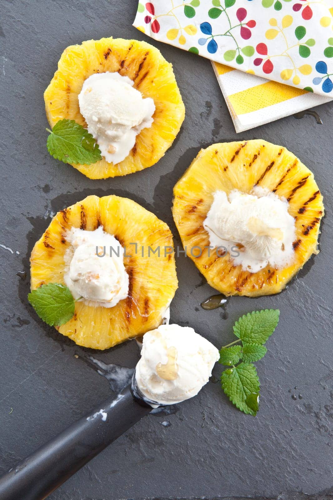 Grilled pineapple rings with ice cream balls and honey on slate plate
