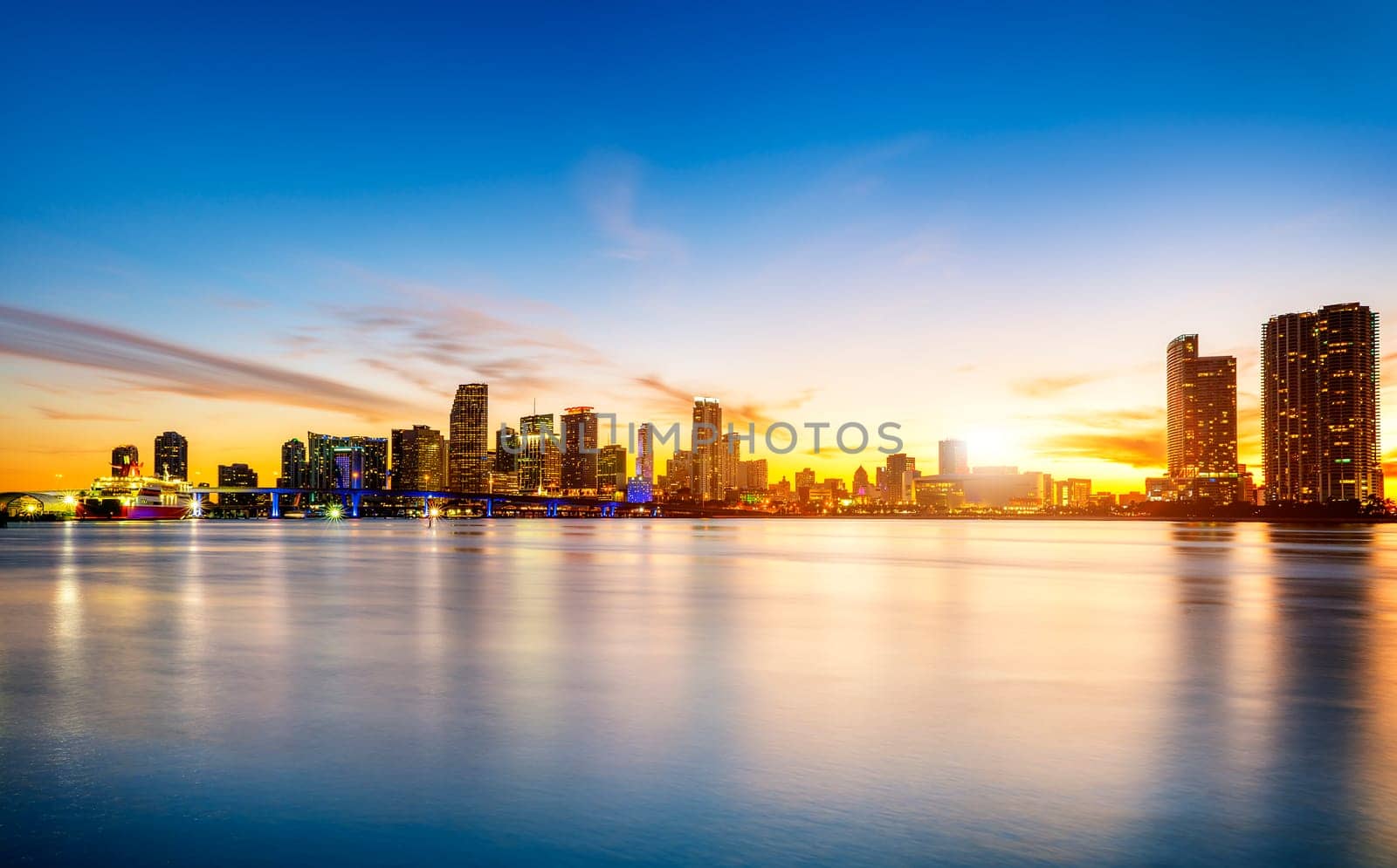 Miami city skyline panorama at dusk with urban skyscrapers over sea with reflection