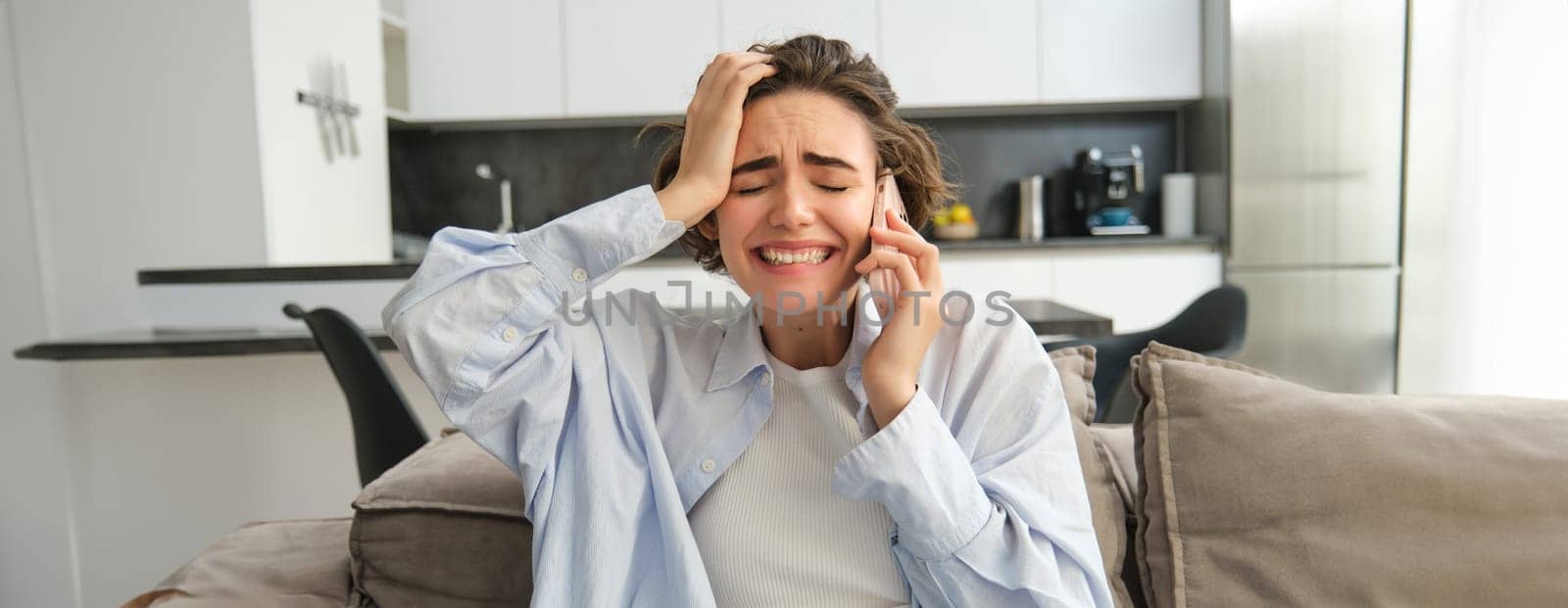 Image of frustrated woman on phone call, listens to bad news during telephone conversation, sits at home, feels disappointed and upset by Benzoix