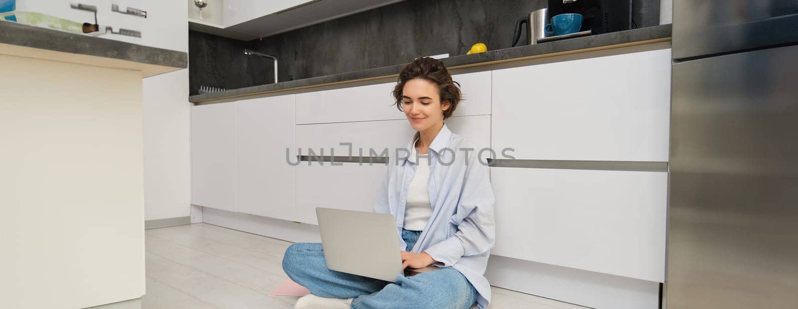 Young woman studying on floor. Girl with laptop works from home, types on computer, smiles and feels creative.