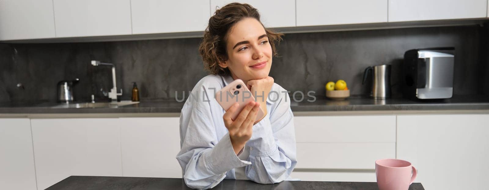 Portrait of beautiful smiling woman sitting at home with smartphone, using mobile phone app, orders groceries delivery by Benzoix