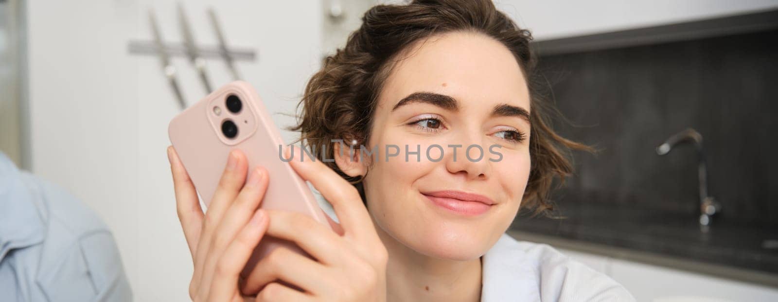 Close up portrait of smiling brunette woman using smartphone, holding mobile phone in hands and looking away, concept of takeaway order, online shopping and communication.