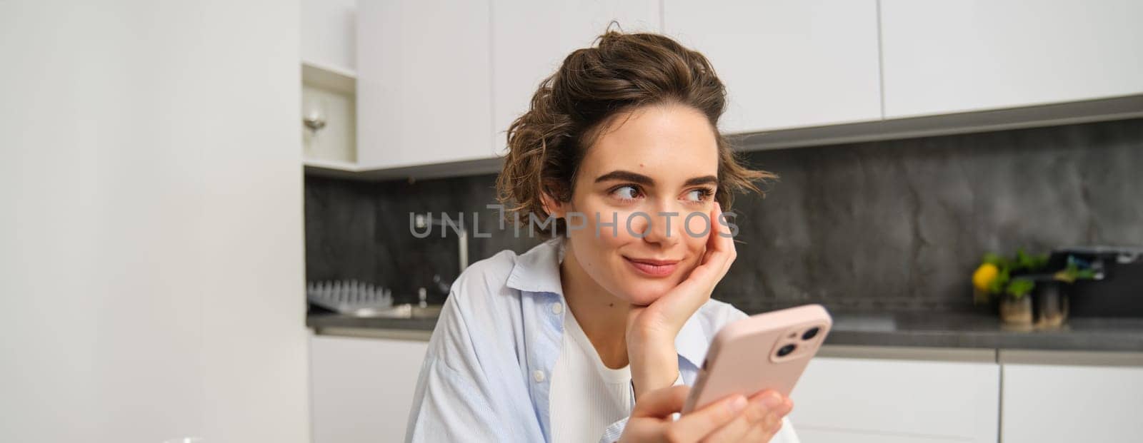 Portrait of woman thinking while holding smartphone, deciding what to order on mobile phone app.