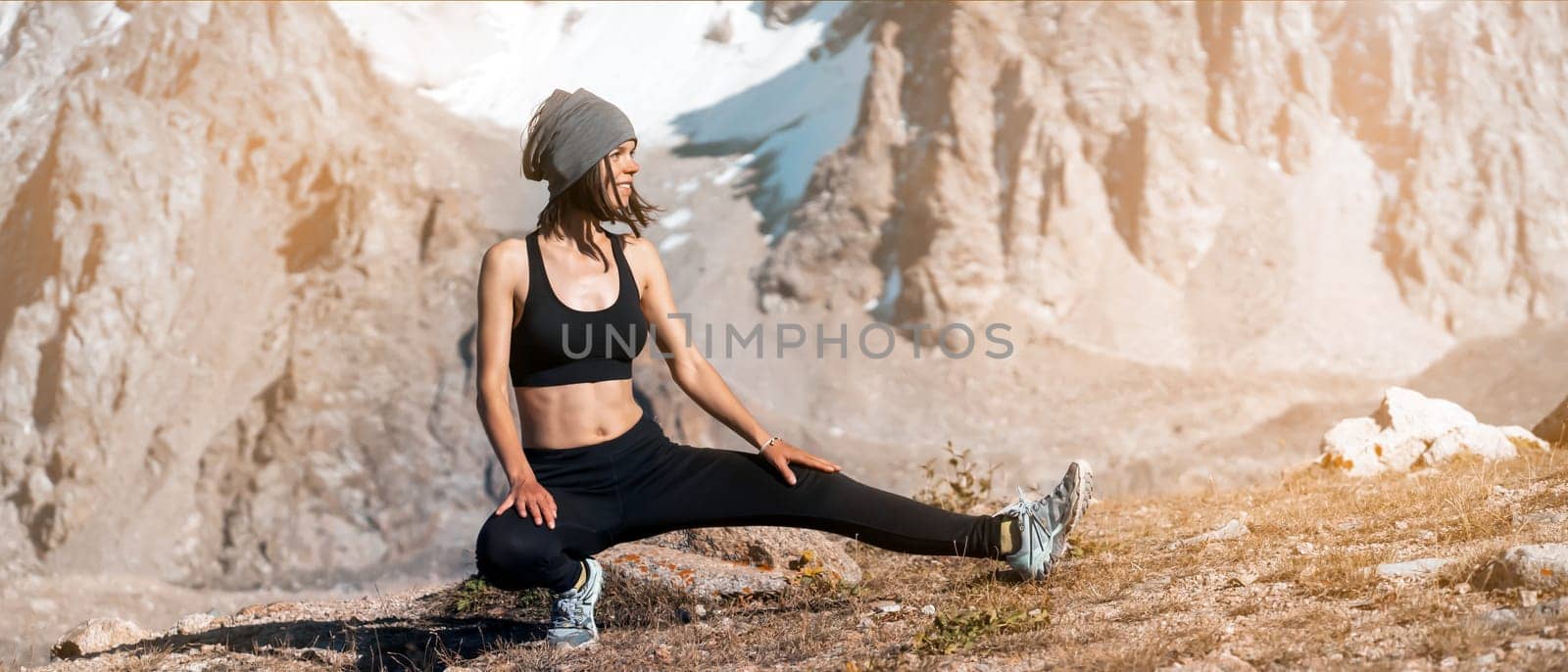 A young sports girl is warming up on a background of snow-capped mountains on a sunny day, a woman does exercises, trains and meditates in a picturesque mountainous area.