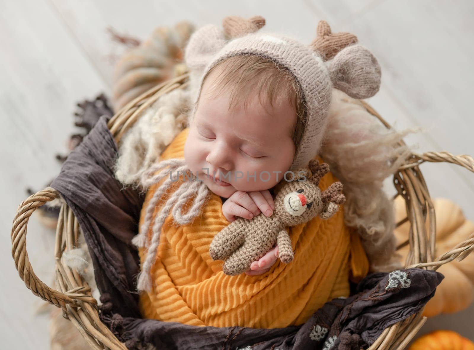 Newborn baby girl swaddled in white fabric sleeping in basket decorated with pumpkins. Infant child kid napping on fur autumn studio portrait