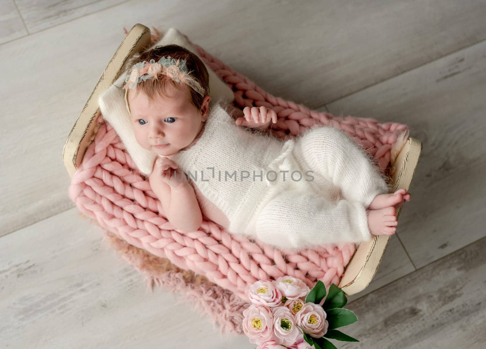 Adorable newborn baby girl lying in tiny bed on fur portrait. Cute infant child kid swaddled in fabric resting in room with daylight