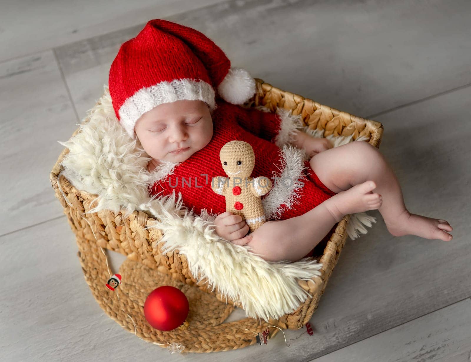 Newborn baby boy wearing Santa Christmas costume sleeping in basket with xmas decoration. Little infant child New Year portrait