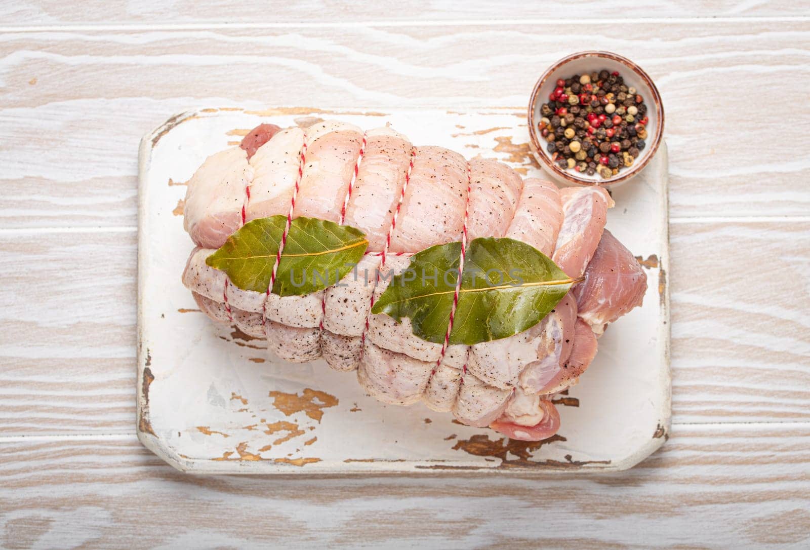 Raw wrapped rolled sliced pork with bay leaf and seasonings on white cutting board on rustic white wooden background top view. Pork roll ready to be prepared by its_al_dente