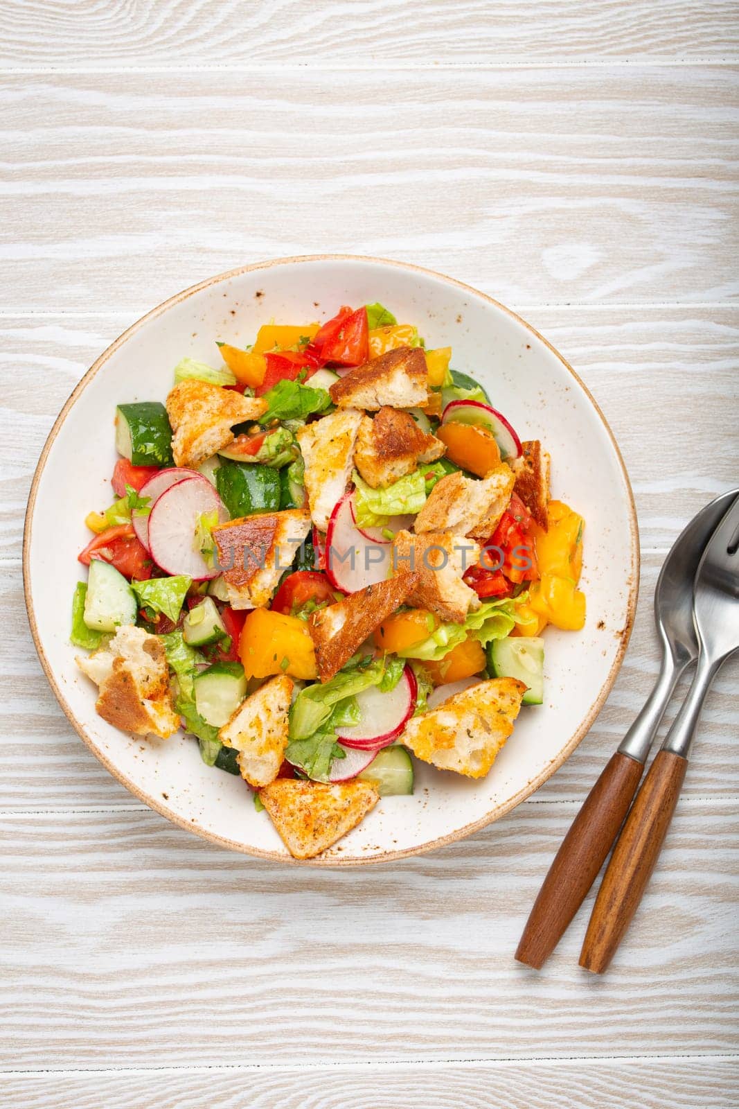 Traditional Levant dish Fattoush salad, Arab cuisine, with pita bread croutons, vegetables, herbs. Healthy Middle Eastern vegetarian salad, rustic wooden white background top view by its_al_dente