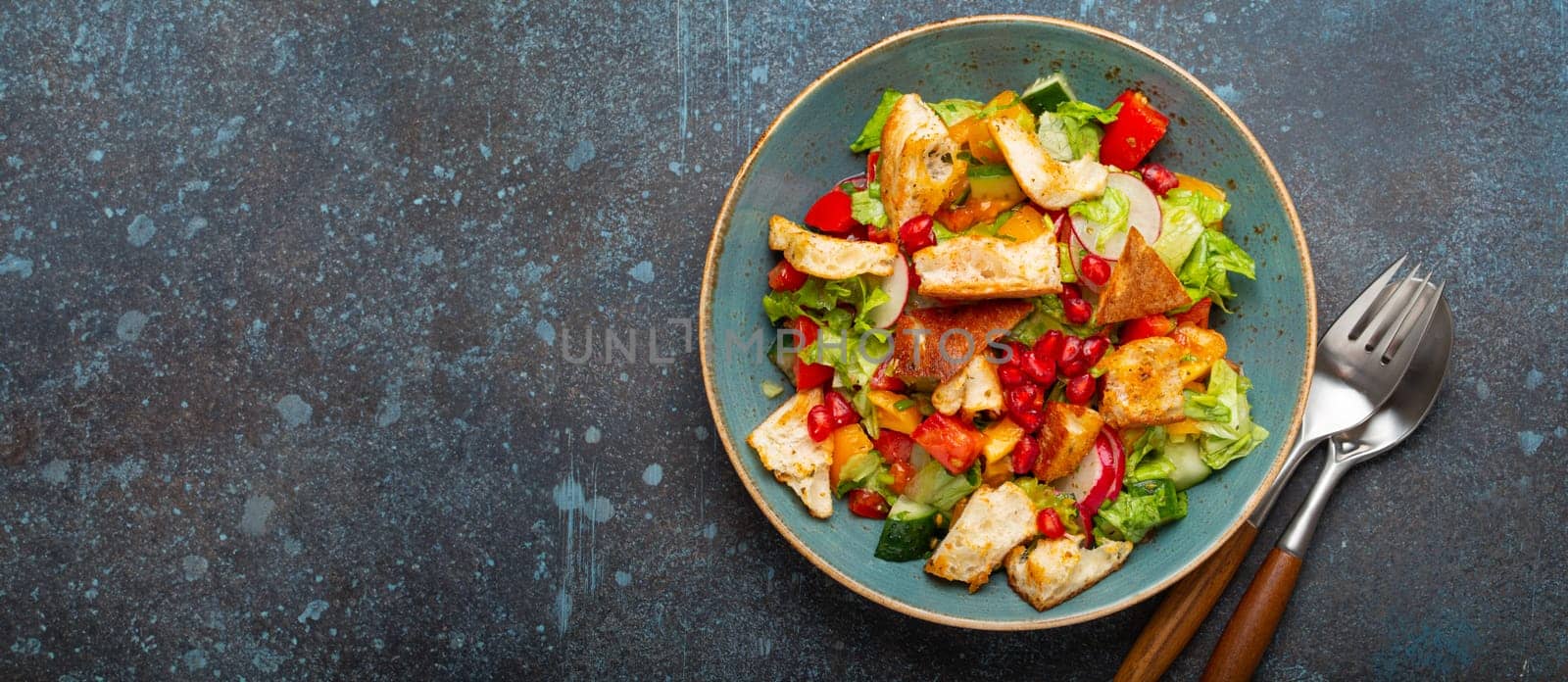 Traditional Levant dish Fattoush salad, Arab cuisine, made with pita bread croutons, vegetables and herbs. Healthy Middle Eastern vegetarian salad on plate, rustic dark blue background top view.