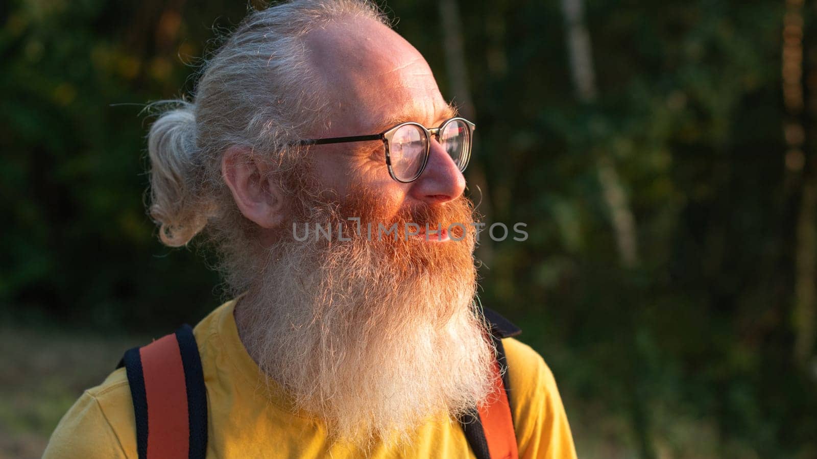 a bearded middle-aged man with glasses in a yellow T-shirt looks at the sunset behind the forest, adventurer, High quality photo