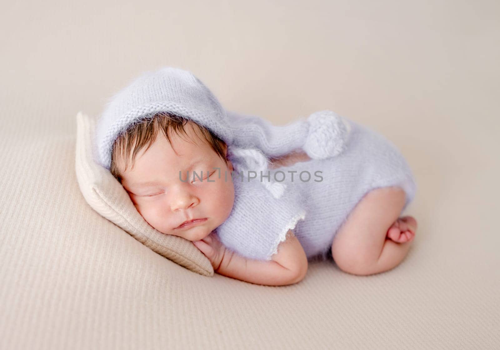 Adorable newborn baby girl sleeping on pillow. Cute infant child kid in knitted dress napping lying on tummy