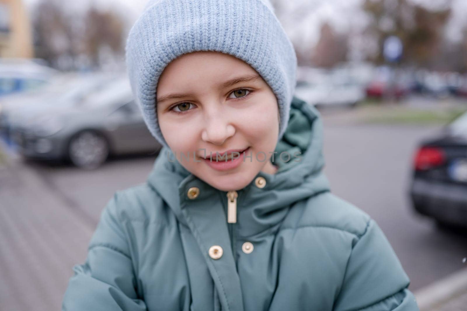 Preteen girl smiling at street portrait in city with blurred background. Cute female child kid wearing hat outdoors at autumn time