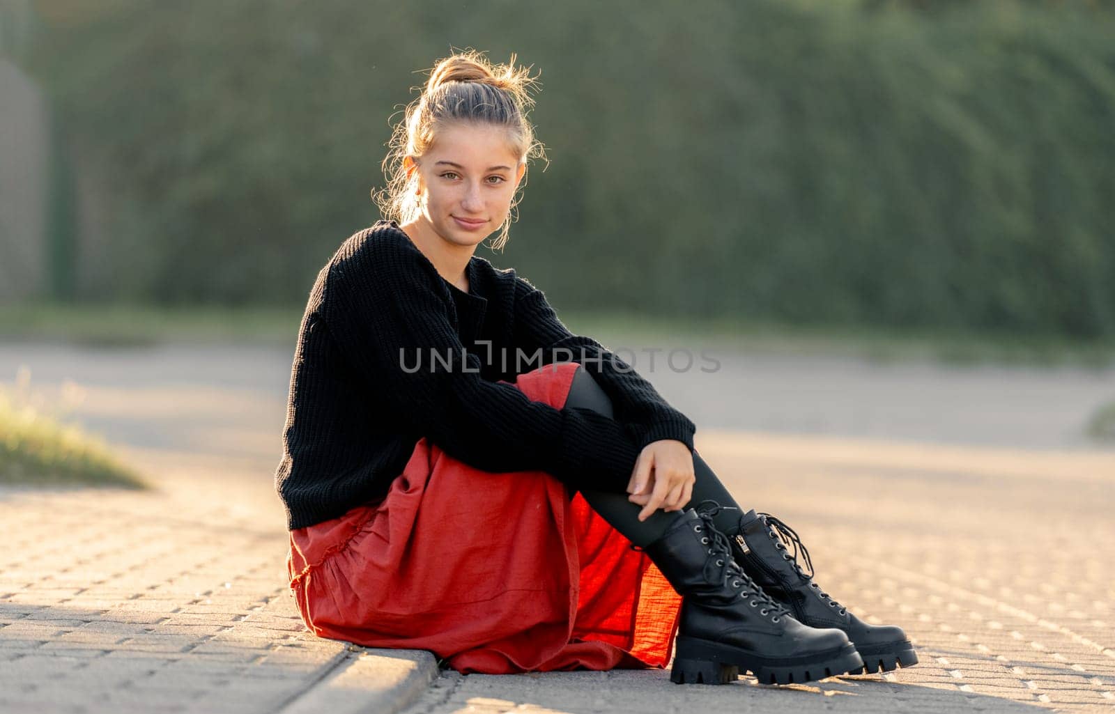 Beautiful teenager girl in red skirt sitting outdoors at street. Pretty teen model posing in trendy clothes