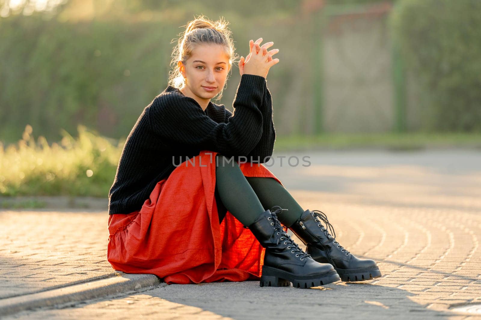 Beautiful teenager girl in red skirt sitting outdoors at street. Pretty teen model posing in trendy clothes