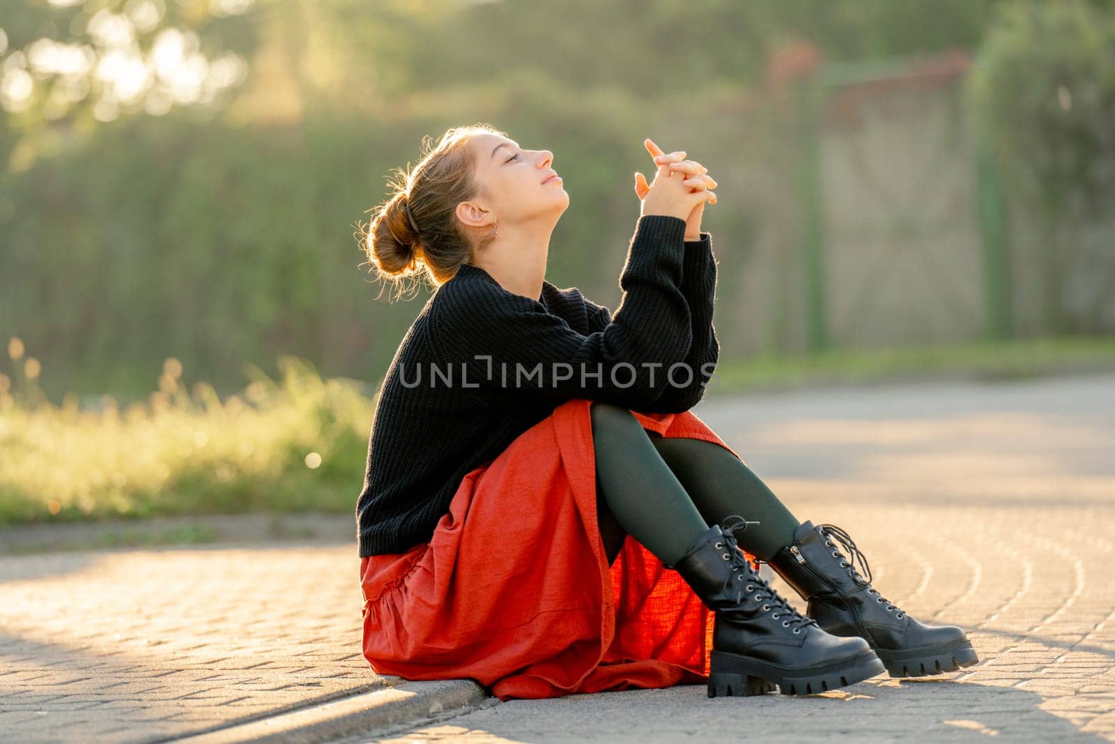 Beautiful teenager girl in red skirt sitting outdoors at street. Pretty teen model posing in trendy clothes