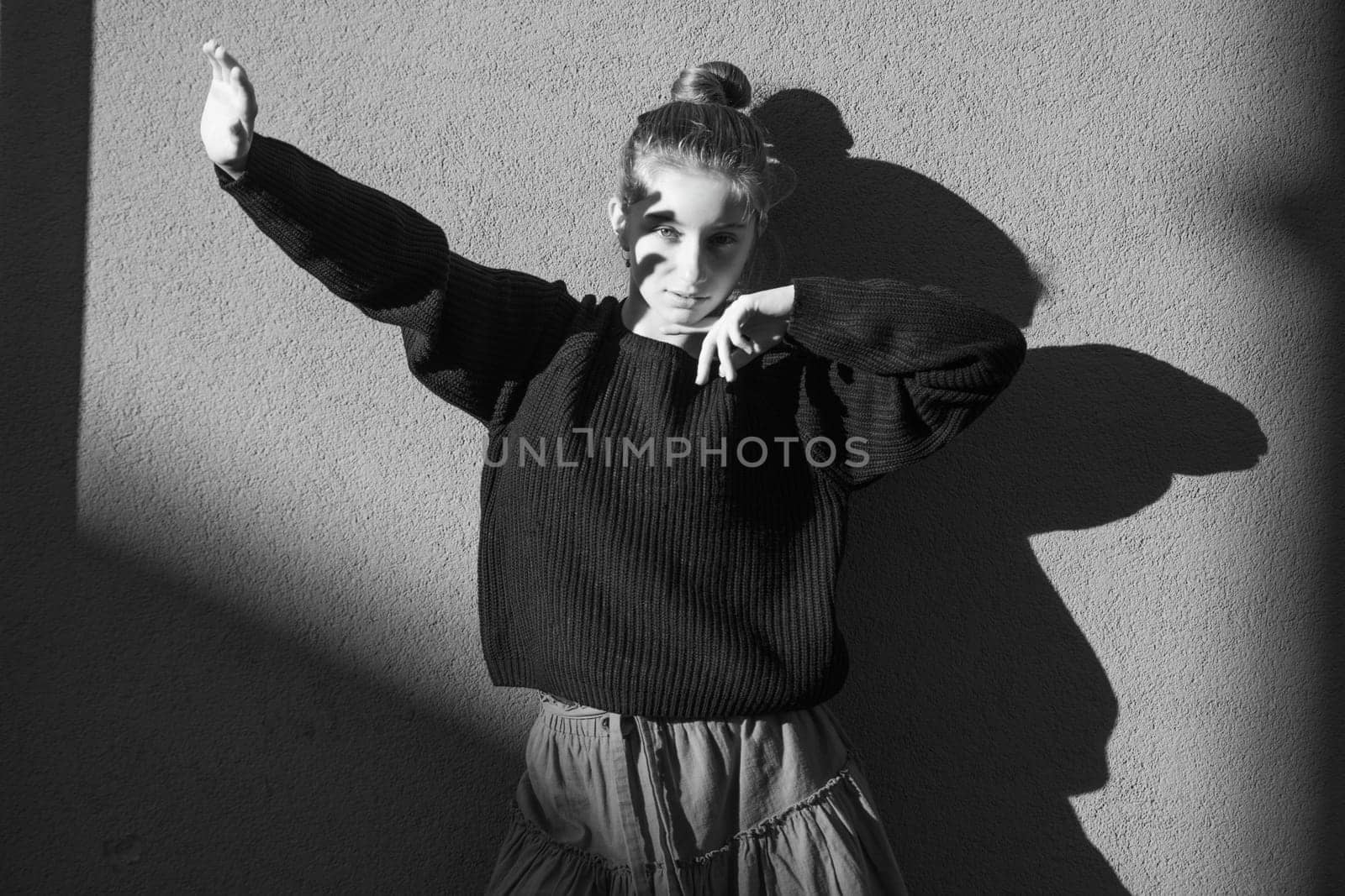 Pretty girl posing near wall with shadows covering face with hand from sunlight. Beautiful teenager model in sun rays at autumn