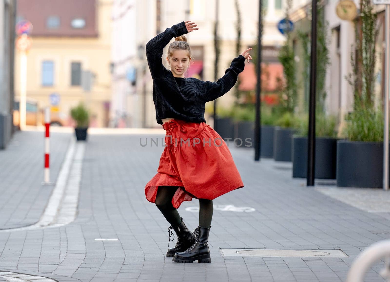 Beautiful teenager girl in red skirt posing at city street with daylight. Pretty teen model in trendy clothes in old town portrait