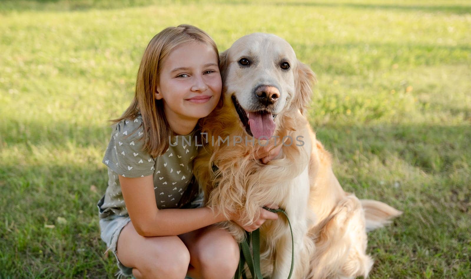 Cute preteen child girl hugging golden retriever dog at nature. Pretty kid with purebred doggy pet labrador at park