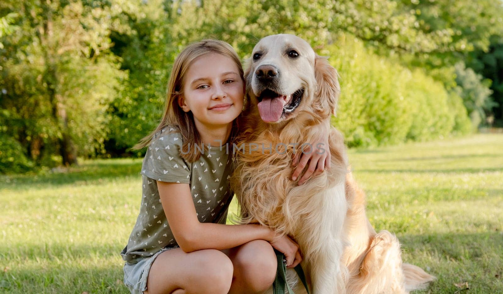 Cute preteen child girl hugging golden retriever dog at nature. Pretty kid with purebred doggy pet labrador at park