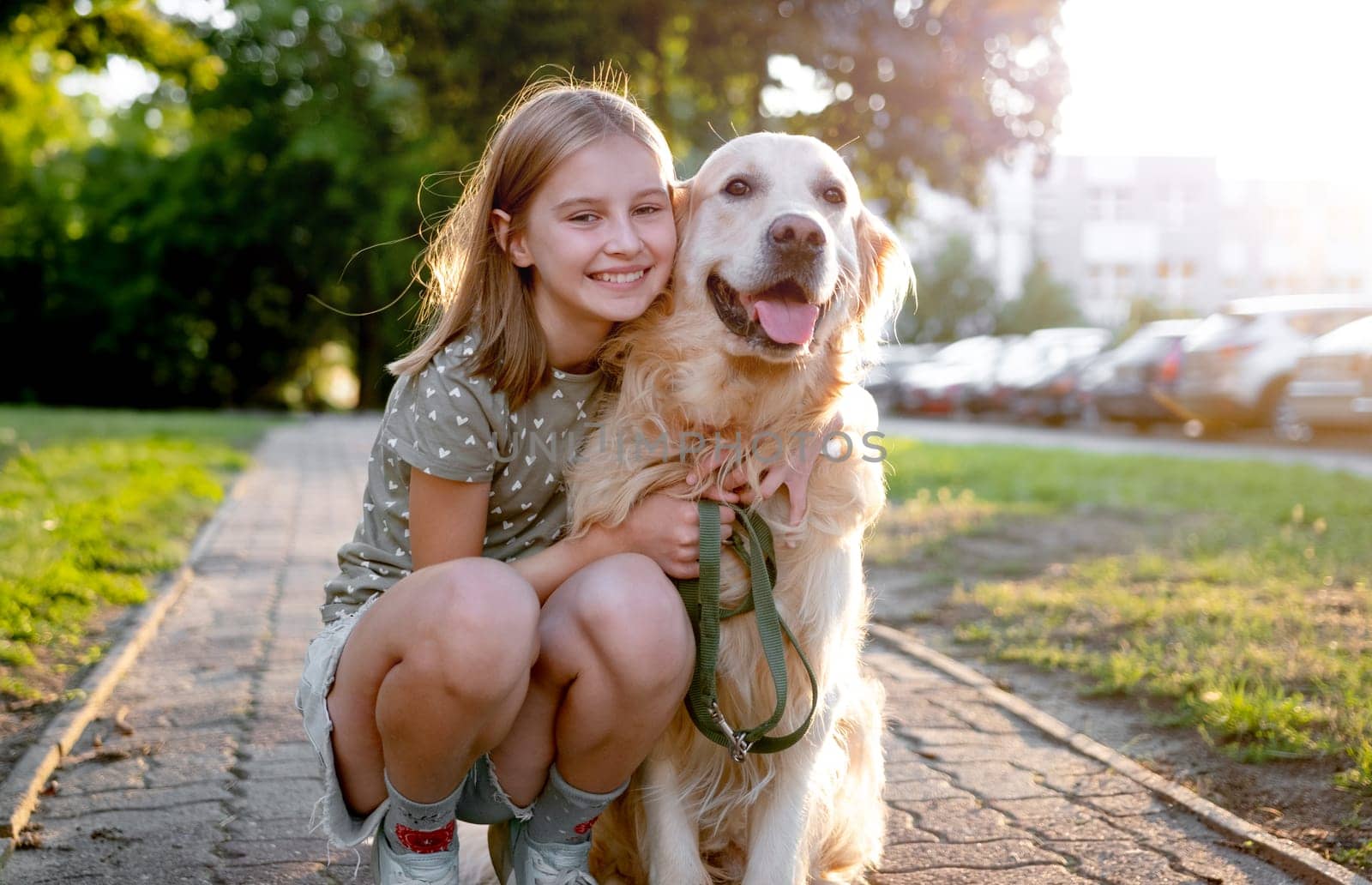 Cute preteen child girl hugging golden retriever dog at nature. Pretty kid petting purebred doggy pet labrador at park and smiling