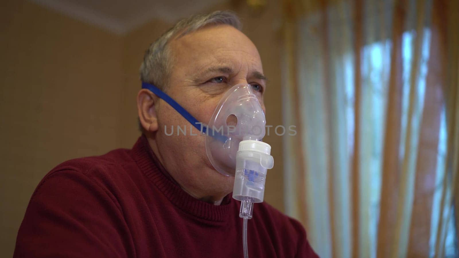 An elderly man inhales through an oxygen mask. A man does a respiratory procedure at home. Closeup. 4k