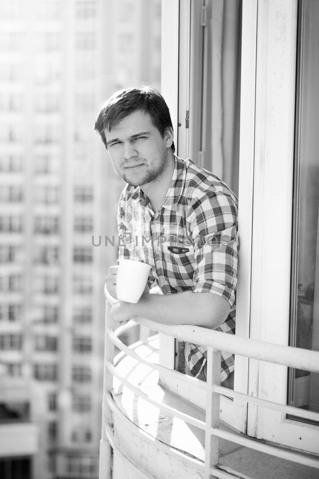 Black and white portrait of man with cup of coffee on balcony