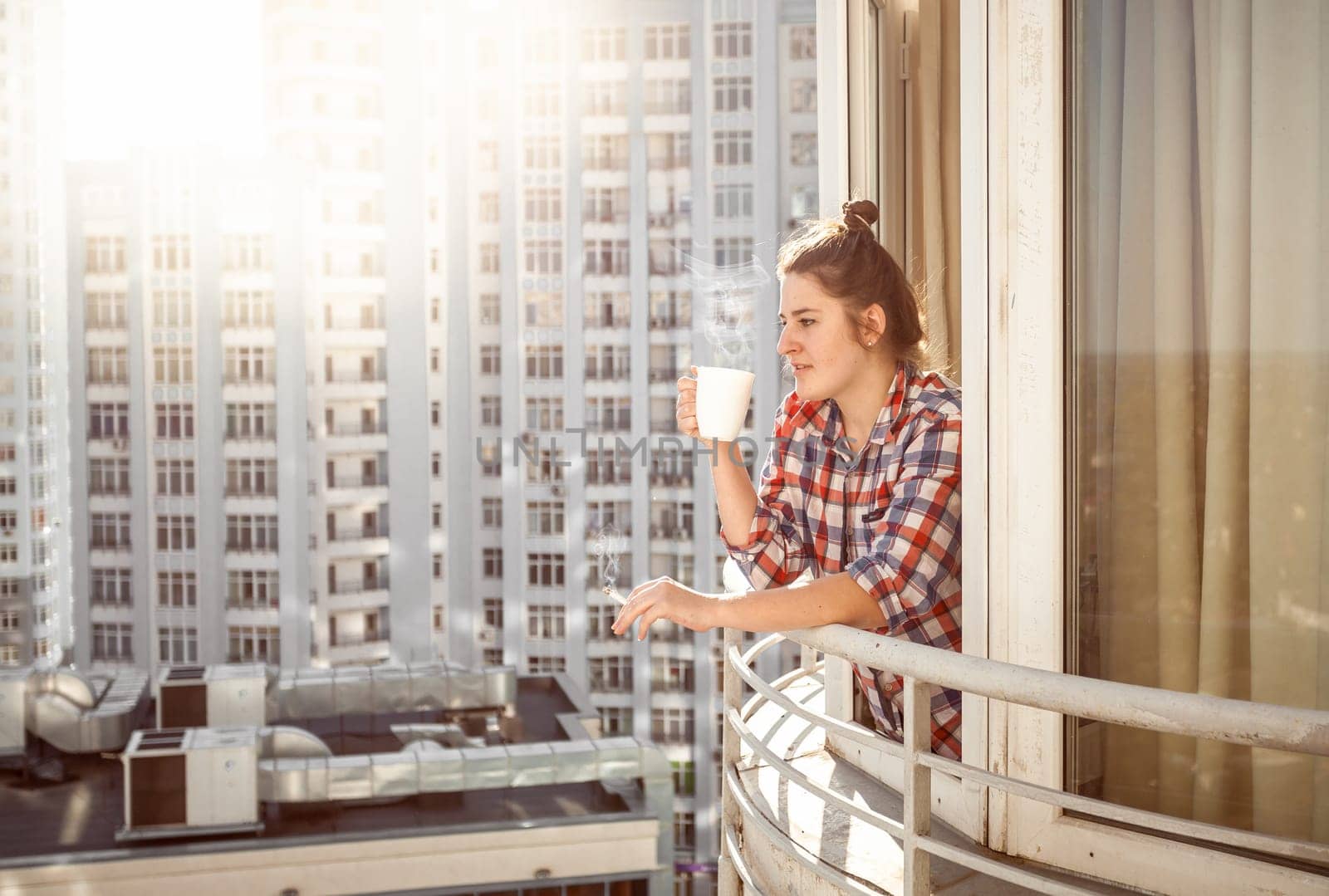 Portrait woman drinking coffee and smoking out of window