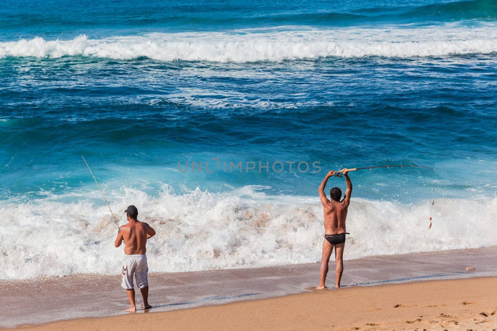 Fishermen casting bait from beach into blue ocean waters on summer afternoon