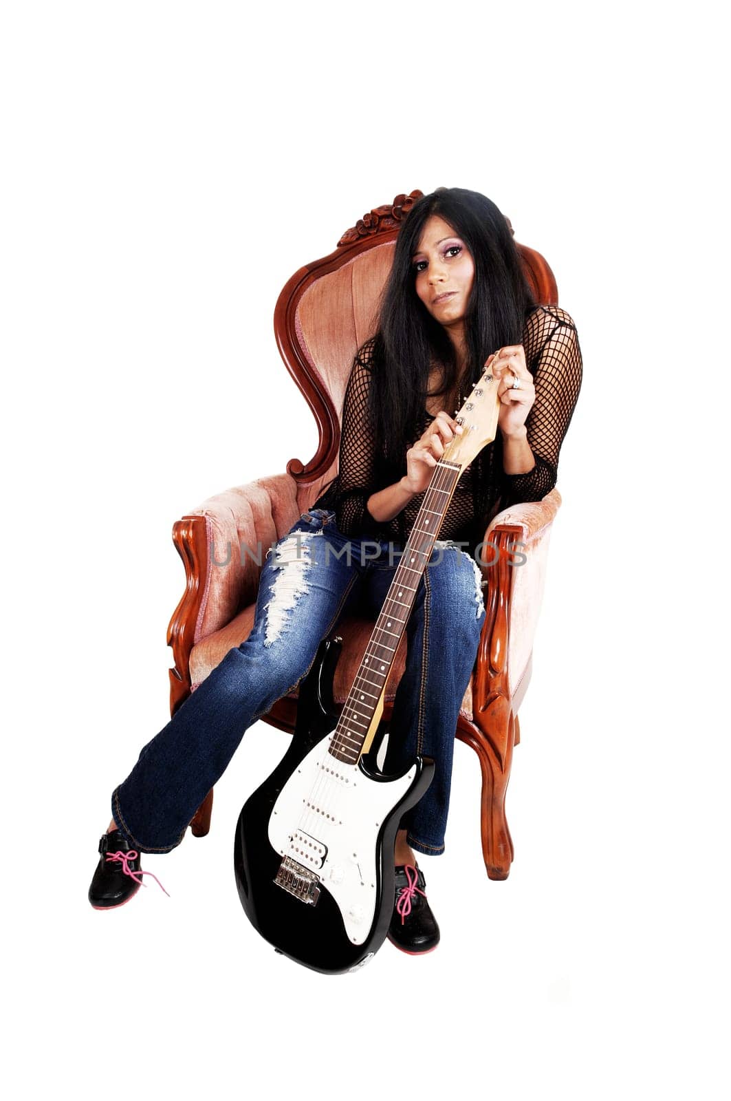 A young pretty Hispanic woman, holding her guitar, sitting in a pink.armchair isolated for white background..