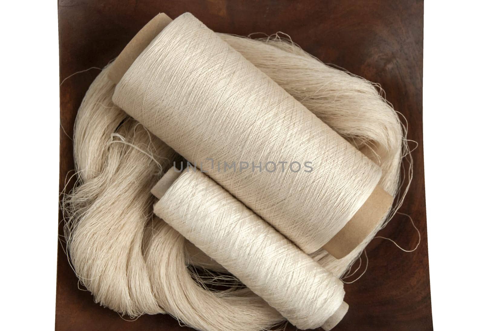 Raw natural silk yarn skein and bobbins in wooden platter isolated on white background