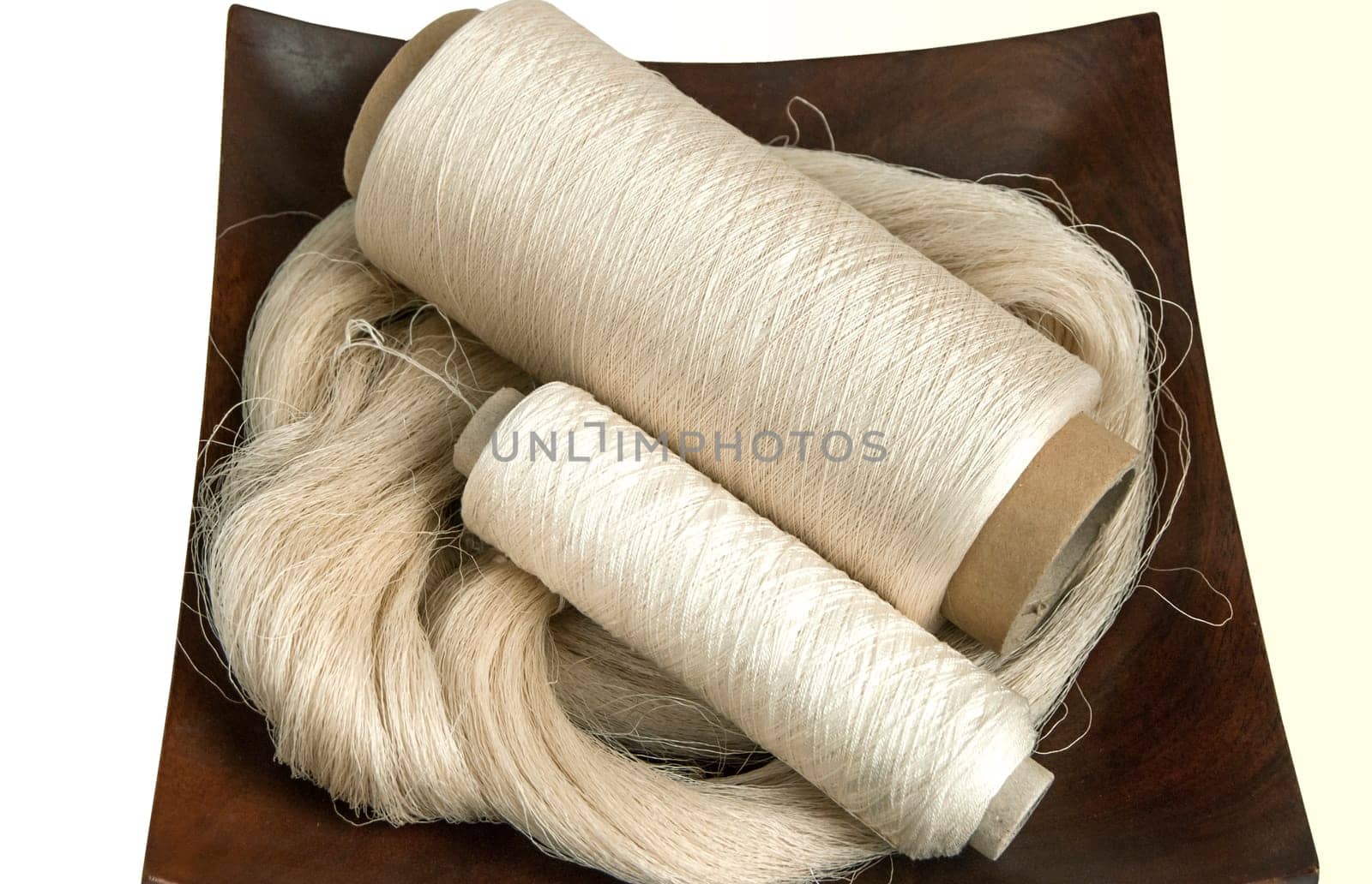 Raw natural silk yarn skein and bobbins in wooden platter isolated on white background