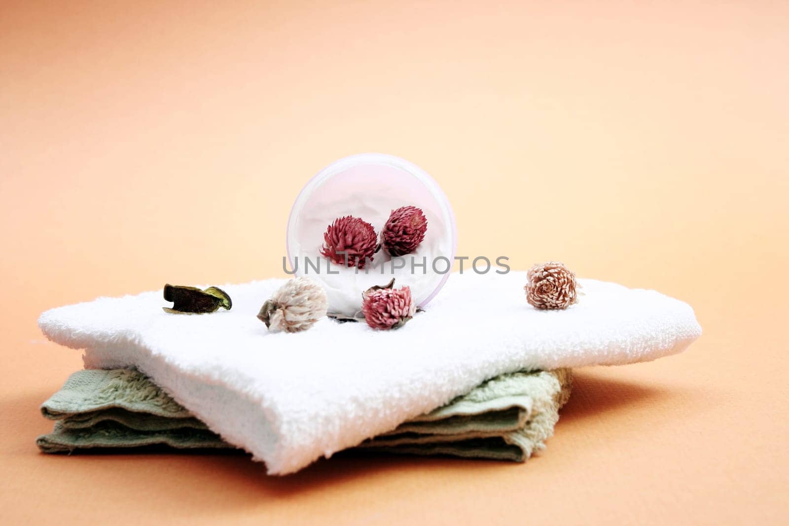 Spa essentials (cream, white towel and pink flowers) isolated on yellow