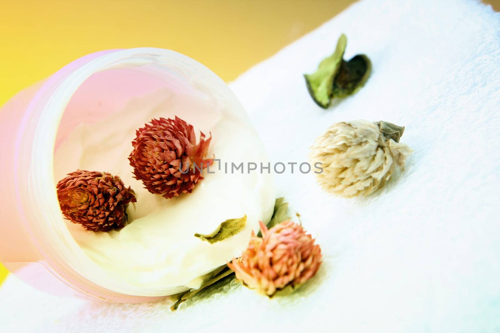 Spa essentials (cream, white towel and pink flowers) isolated on yellow